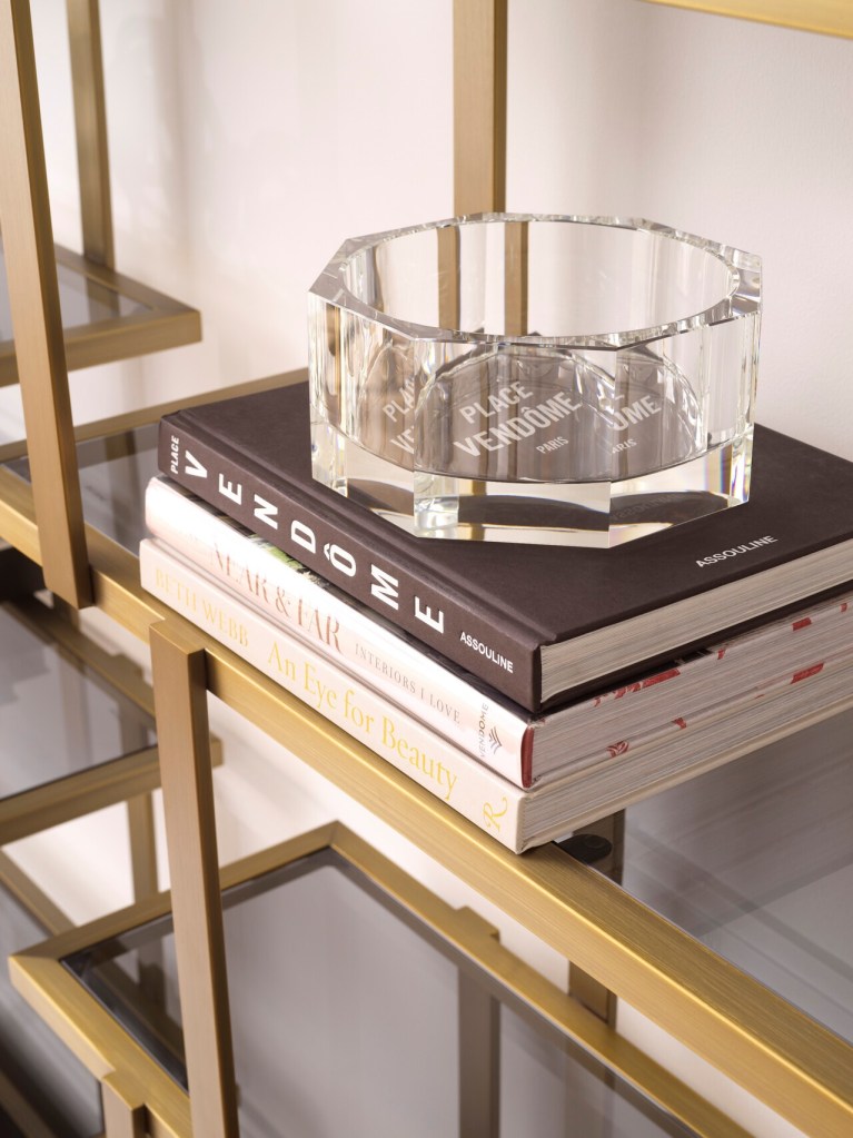 Clear glass bowl on top of stacked decorative books, placed on a gold metal shelf.